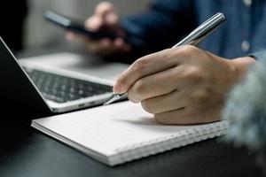 Man hand with pen writing on notebook with computer laptop at desk. photo