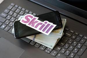 TERNOPIL, UKRAINE - SEPTEMBER 6, 2022 Skrill paper logotype lies on black laptop with US dollar bills. Payoneer is American financial services company provides online money transfer photo