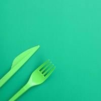 Disposable plastic cutlery green. Plastic fork and knife lie on a green background surface photo