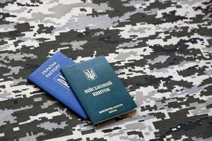 SUMY, UKRAINE - MARCH 20, 2022 Ukrainian military ID and foreign passport on fabric with texture of pixeled camouflage. photo