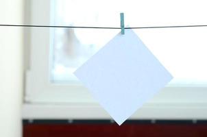 White blank card on rope, window glass background. Creative reminder, small sheet of paper on wooden clothespin, memo backdrop photo