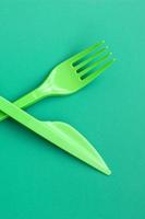 Disposable plastic cutlery green. Plastic fork and knife lie on a green background surface photo