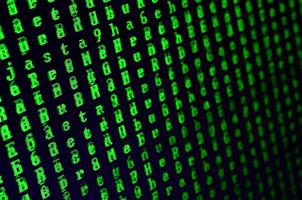 Macro shot of a glitch on the monitor of an office computer. The concept of introducing a virus into a personal data keeper. Stream of random green symbols on a black background photo