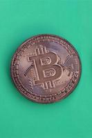 Chocolate product in the form of physical bitcoin lies on a green plastic background. Model of the crypto currency in the edible form photo