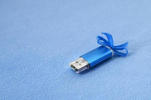 la tarjeta de memoria flash usb azul brillante con un lazo azul se encuentra sobre una manta de tela de vellón azul claro suave y peluda. diseño clásico de regalo femenino para una tarjeta de memoria foto