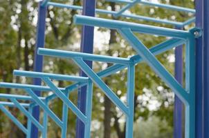 Blue metal pipes and cross-bars against a street sports field for training in athletics. Outdoor athletic gym equipment. Macro photo with selective focus and extremely blurred background