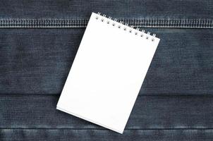 White notebook with clean pages lying on dark blue jeans background. Image with copy space photo