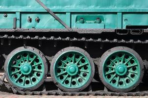 Side view of the vehicle on a caterpillar track with black tracks and green wheels and a side metal wall photo