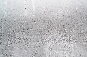 textura de una gota de lluvia sobre un fondo transparente húmedo de vidrio. tonificado en color gris foto