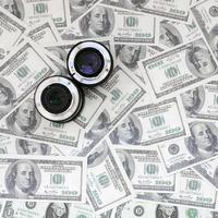 Two photographic lenses lie on the background of a lot of dollar bills. Space for text photo