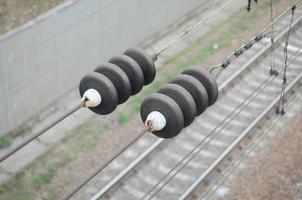 Electrical insulators on the contact wires on the background of a blurred railway track. Macro photo with selective focus