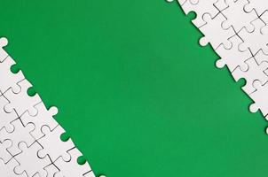 Fragment of a folded white jigsaw puzzle on the background of a green plastic surface. Texture photo with copy space for text