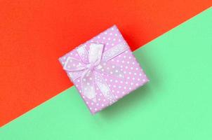 Small pink gift box lie on texture background of fashion pastel turquoise and red colors paper photo