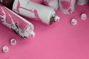 Some used pink aerosol spray cans and nozzles with paint drips lies on a blanket of soft and furry light pink fleece fabric. Classic female design color. Graffiti hooliganism concept photo