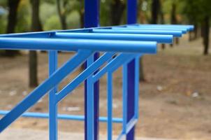 tubos de metal azul y barras transversales contra un campo de deportes callejeros para entrenar en atletismo. equipo de gimnasia atlética al aire libre. foto macro con enfoque selectivo y fondo extremadamente borroso