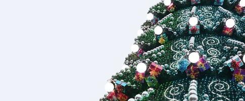 A fragment of a huge Christmas tree with many ornaments, gift boxes and luminous lamps. Photo of a decorated Christmas tree close-up with copy space