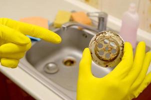 Cleaner in rubber gloves shows waste in the plughole protector of a kitchen sink photo