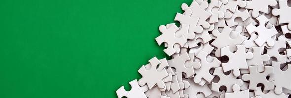 A pile of uncombed elements of a white jigsaw puzzle lies on the background of a green surface. Texture photo with copy space for text