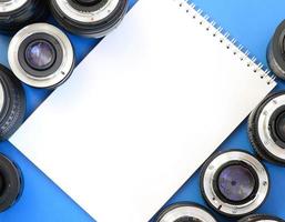 Several photographic lenses and white notebook lie on a bright blue background. Space for text photo