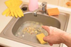 Hand points to dirty kitchen sink with many food particles before the cleaning photo