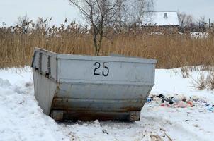 Trash bin at the side of street in winter with lip garbage container winter snow. Metal container for household waste photo