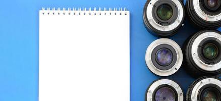 Several photographic lenses and white notebook lie on a bright blue background. Space for text photo