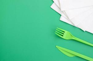 Disposable plastic cutlery green. Plastic fork and knife lie on a green background surface next to napkins photo