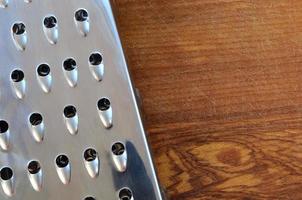 The chrome grater lies on the cutting board with a lot of scars from the ax and knife. Background image for cooking recipes photo