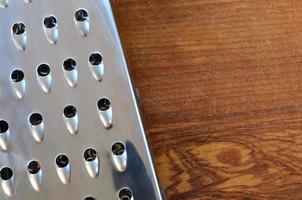 The chrome grater lies on the cutting board with a lot of scars from the ax and knife. Background image for cooking recipes photo