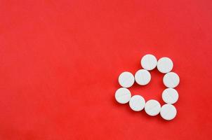 Several white tablets lie on a bright red background in the shape of a heart. Background image on medicine and pharmaceutical topics photo