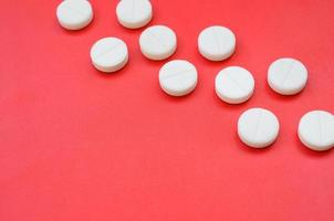 A few white tablets lie on a bright red background surface. Background image on medical and pharmaceutical topics photo