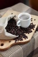 A full bag of brown coffee beans and a white cup of hot coffee l photo