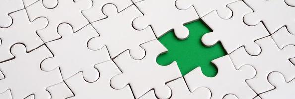 Close-up texture of a white jigsaw puzzle in assembled state with missing elements forming a green pad for text. Copy space photo