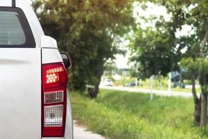 Back side of pick up car white color on the road with turn on brake light.  background image of a green grass and trees. and blurred of car on road far away. photo