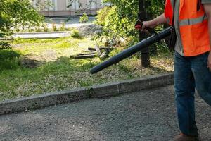 limpiando las hojas que caen en el parque de la ciudad durante el tiempo seco soleado de primavera. usando un soplador para limpiar en el parque. el concepto de trabajo estacional. foto