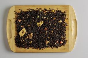 té negro con cítricos secos, plátano y pétalos de flores. fondo de té fragante en una tabla de madera foto