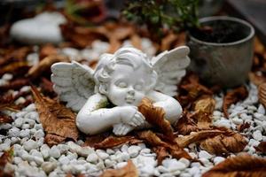 A small angel figure lies sleeping on a grave with autumn leaves