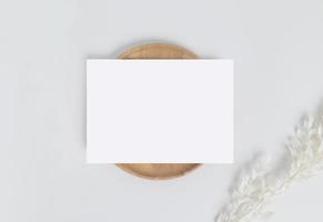 Greeting card or invitation card with white dry flower leaves on wood plate or tray in white background, top view mock up for design photo