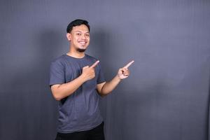 joven atractivo hombre asiático sonriente en camiseta posando aislado sobre fondo gris, espacio de copia simulada. foto