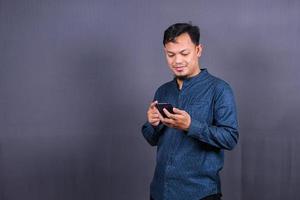 Happy asian man typing sms on gray background. isolated, business concept photo