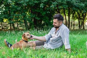 Handsome man in sunglasses sitting on grass with his dog in park. Concept of human and pet relationship. photo