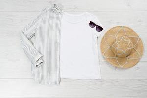 camiseta blanca de primer plano maqueta plana sobre fondo de madera. accesorios de verano. sombrero, gafas de sol. vista superior y espacio de copia. camiseta de maqueta y verano. camisa en blanco de plantilla. foto