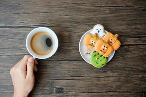 hand holding coffee cup during eating funny Halloween Cookies. Happy Halloween day, Trick or Threat, Hello October, fall autumn, Traditional, party and holiday concept photo