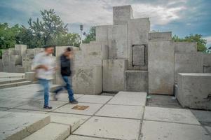 dos personas caminando, larga exposición borrosa, en el fondo escultura de piedra diferentes niveles foto