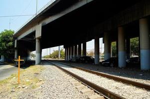 view of the lower part of a bridge for cars, showing the railroad tracks and a yellow cross on the left side. photo