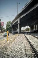 view of the lower part of a bridge for cars, showing the railroad tracks and a yellow cross on the left side. photo