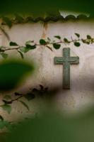 Cross Religion. Symbol. Worship. cross on worn wall among vegetation, plant out of focus and tiles on the top, mexico photo