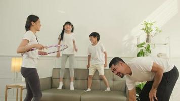 gelukkig welzijn Aziatisch Thais familie, ouders, en kinderen zijn pret spelen hula hoepels samen, geschiktheid opleiding en gezond oefening in wit leven kamer, huiselijk huis levensstijl, en weekend werkzaamheid. video