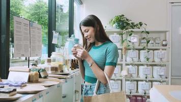 Young Caucasian female customer is choosing and shopping for organic products in refill store with reusable bag, zero-waste grocery, and plastic-free, eco environment-friendly, sustainable lifestyles. video