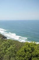 view from a hill overlooking the sea, waves crashing on the beach photo